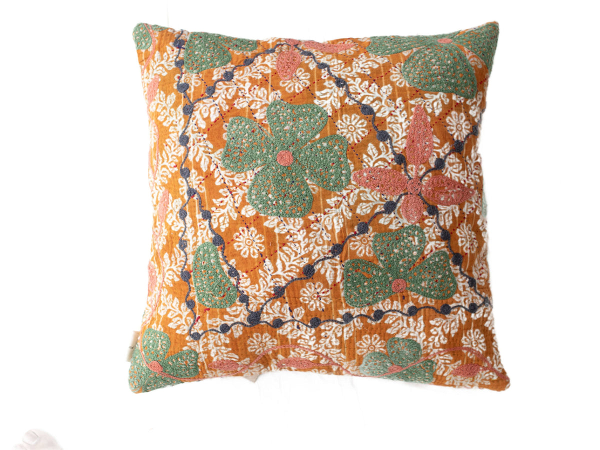 Suzani pillowcase in boho vintage style with orange base and white floral ornaments as well as large green leaves with pink dots and dark blue winding tendrils.
